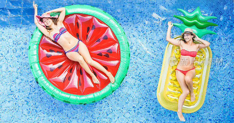 快乐的女孩漂浮在游泳池里的热带水果lilos -年轻的女性朋友放松在度假酒店的暑假-旅游，寒冷，假期，青年概念-温暖过滤器